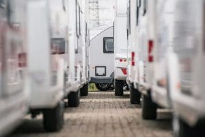 RV dealership lot with multiple white travel trailers and motorhomes parked in rows