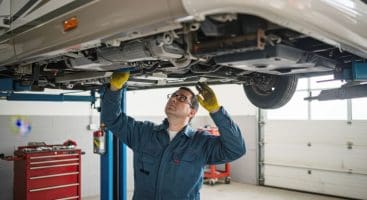 Mechanic inspecting the underside of an RV on a vehicle lift in a service garage.