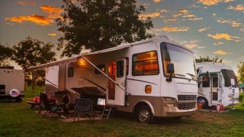 RV campsite at sunset with outdoor chairs and awning set up beside a parked motorhome.